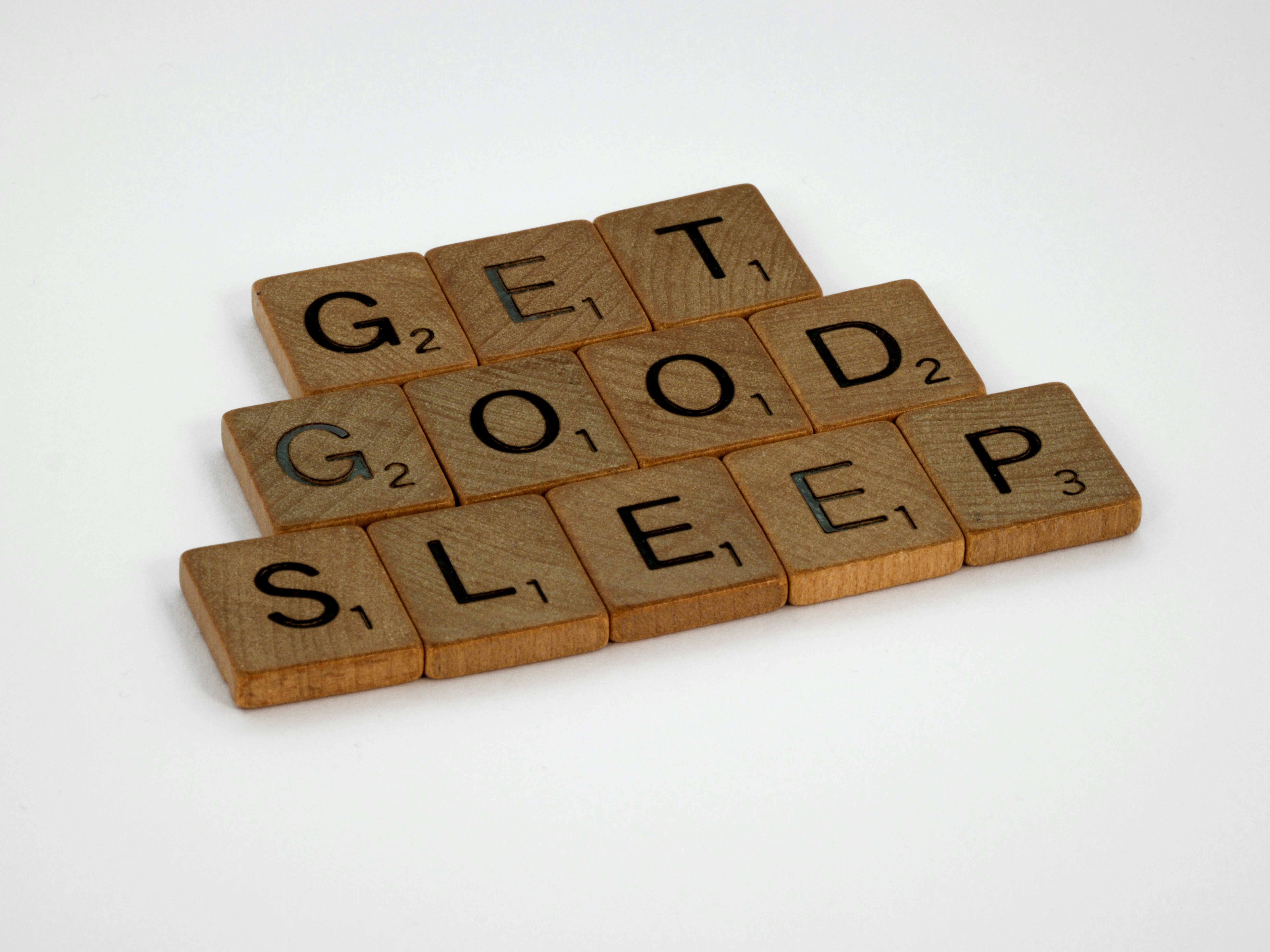 Wooden Scrabble tiles arranged to spell the phrase Get Good Sleep on a white background