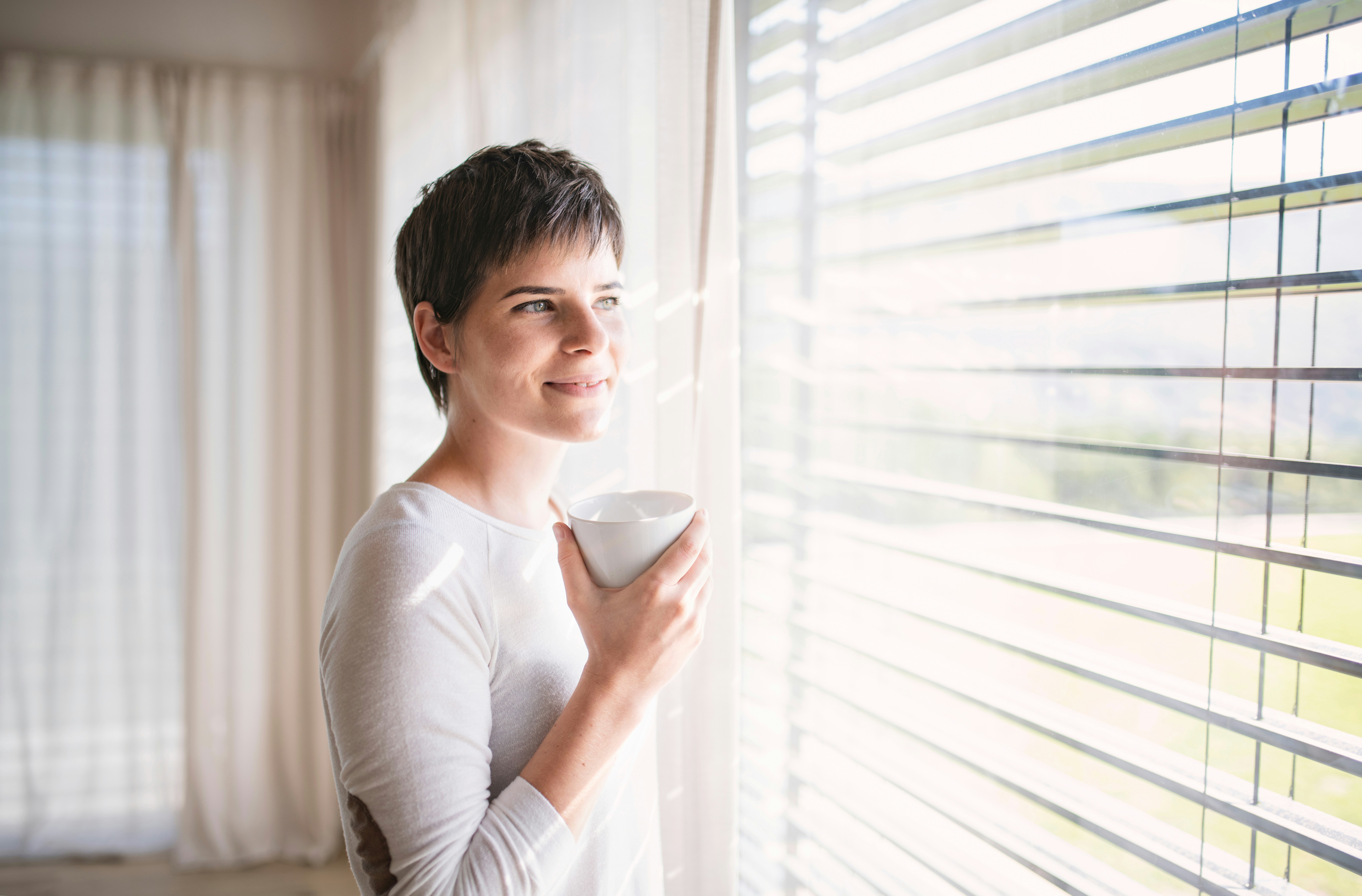 A mature woman holding a cup by a bright window, illustrating perimenopause and sleep changes