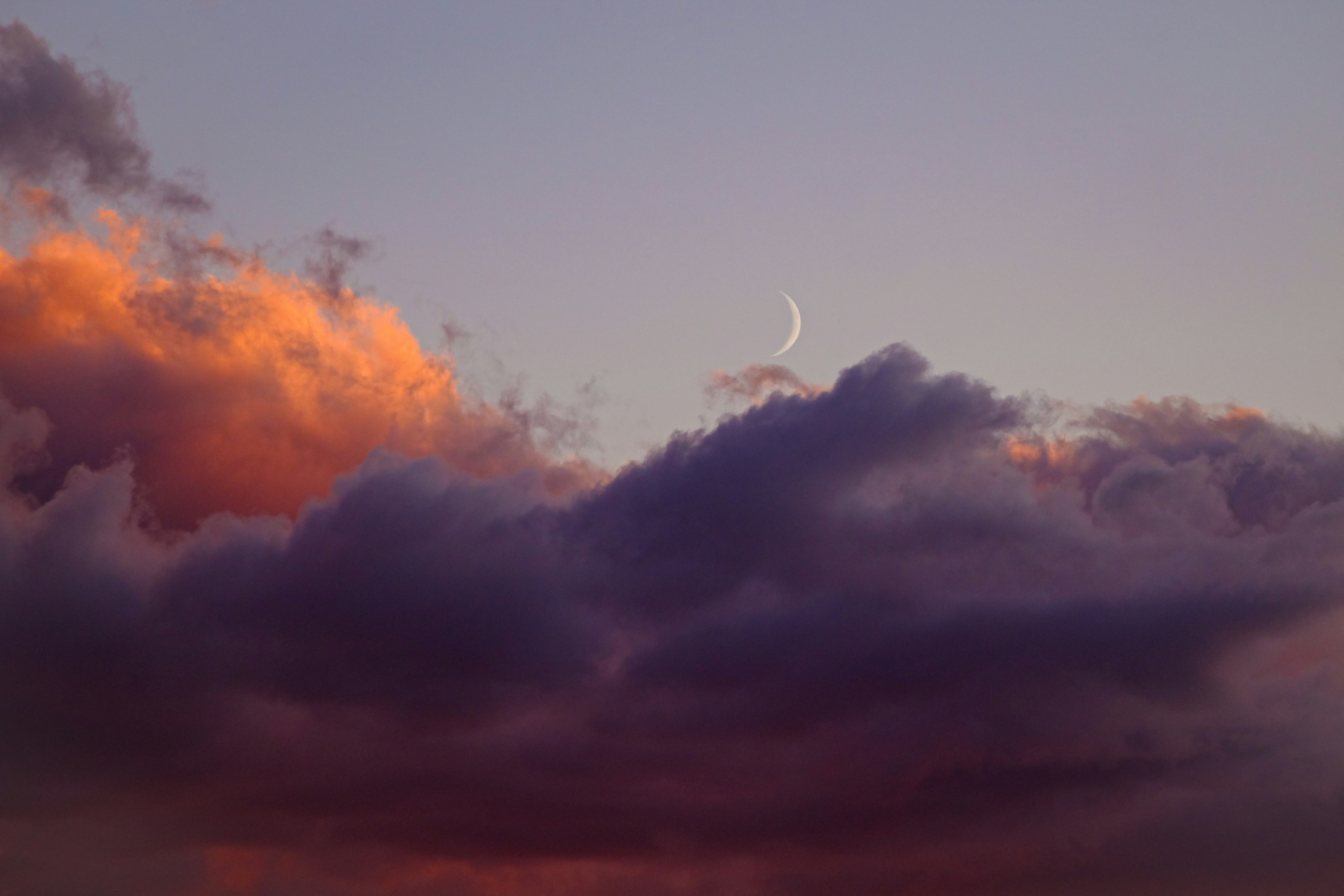 A crescent moon rising over warm sunset clouds on a hot summer evening, representing the challenge of sleeping through warm nights